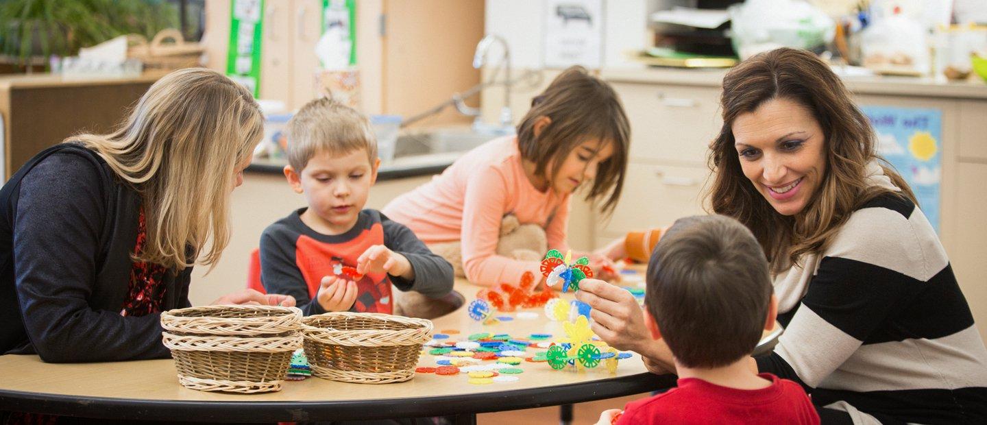 两名女教师和三名年轻的学生在教室里玩着五颜六色的玩具.