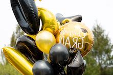 图片上有大小不一的黑色和金色气球，其中有祝贺毕业的文字! 在它上面